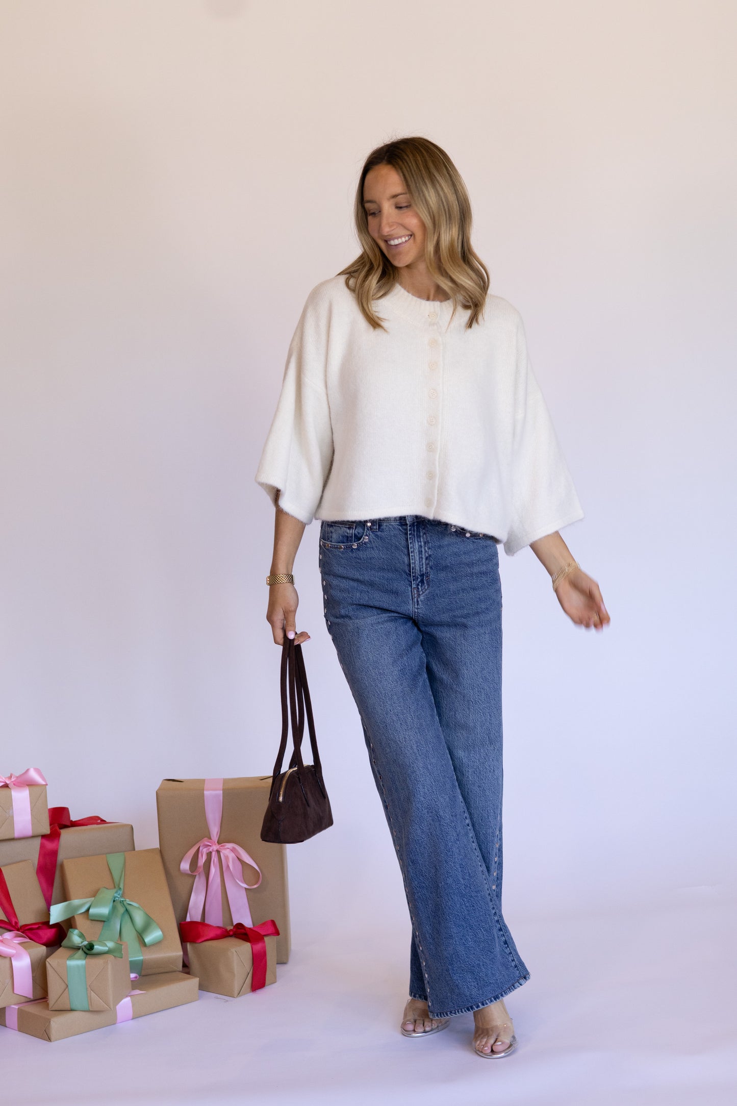 Woman in a white top and blue jeans standing next to gift boxes on a white background