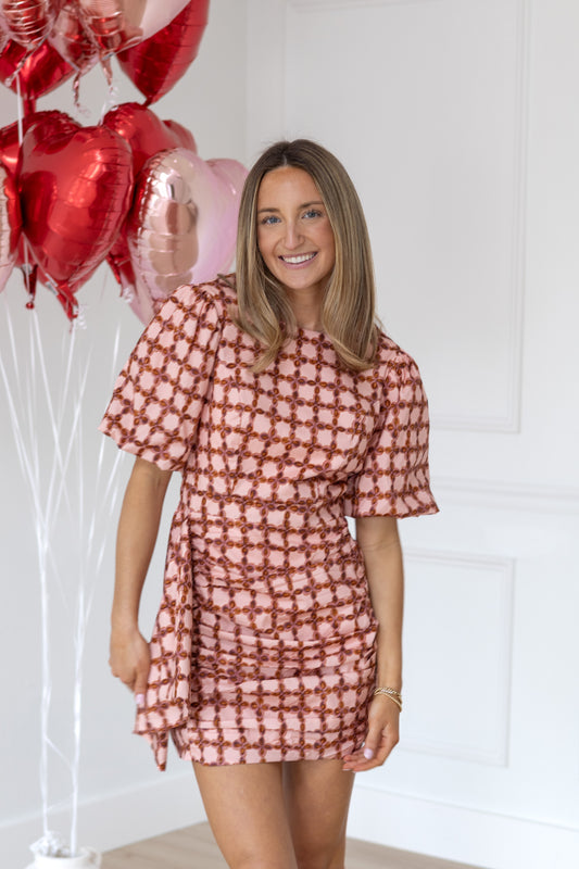 Woman in a patterned dress standing next to red heart-shaped balloons against a white background