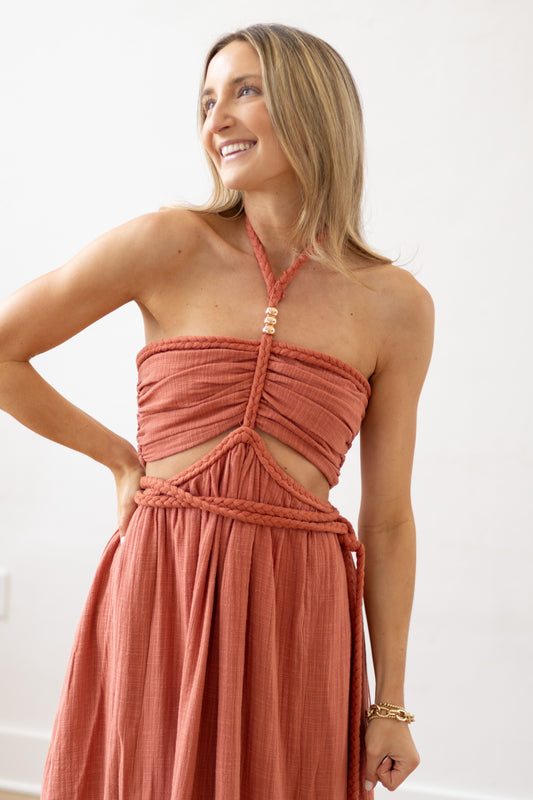 Woman wearing a coral halter neck dress with cut-out design against a white background