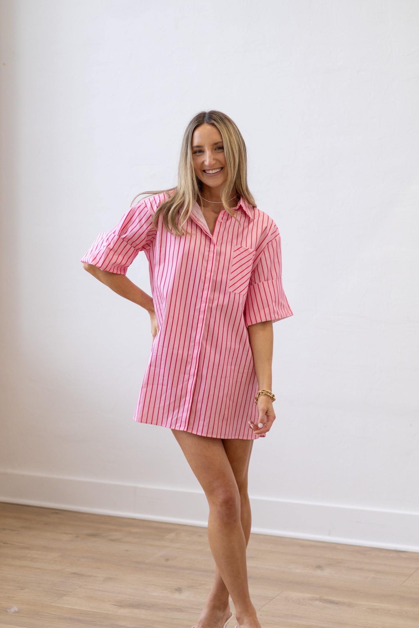 Woman wearing a pink and white striped dress against a white wall.