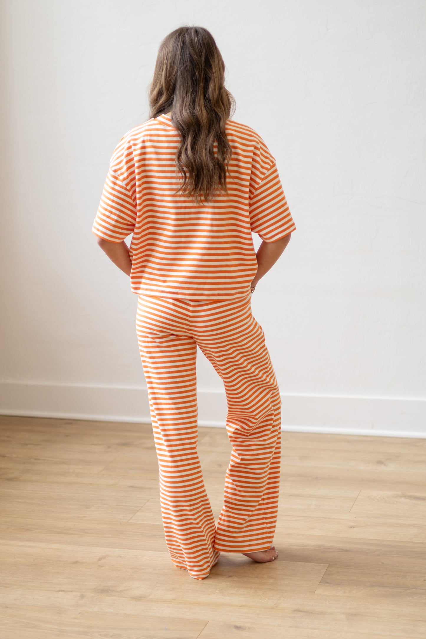 Person wearing orange and white striped pajamas standing on a wooden floor with a white wall background