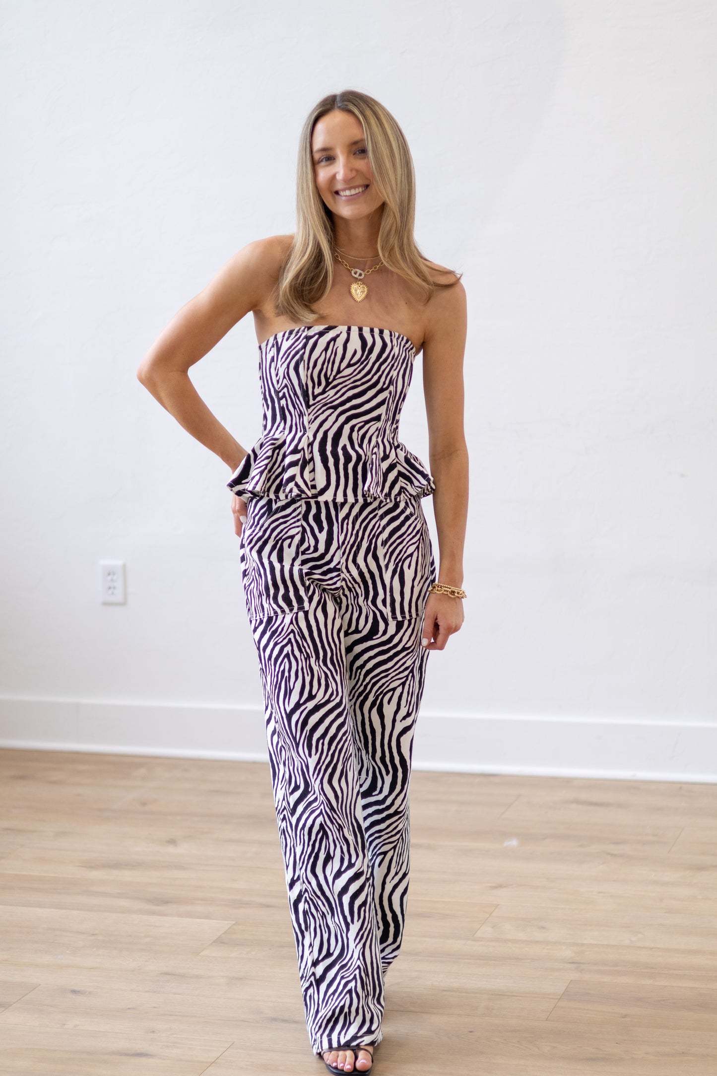 Woman wearing a zebra print strapless jumpsuit in a room with wooden flooring.