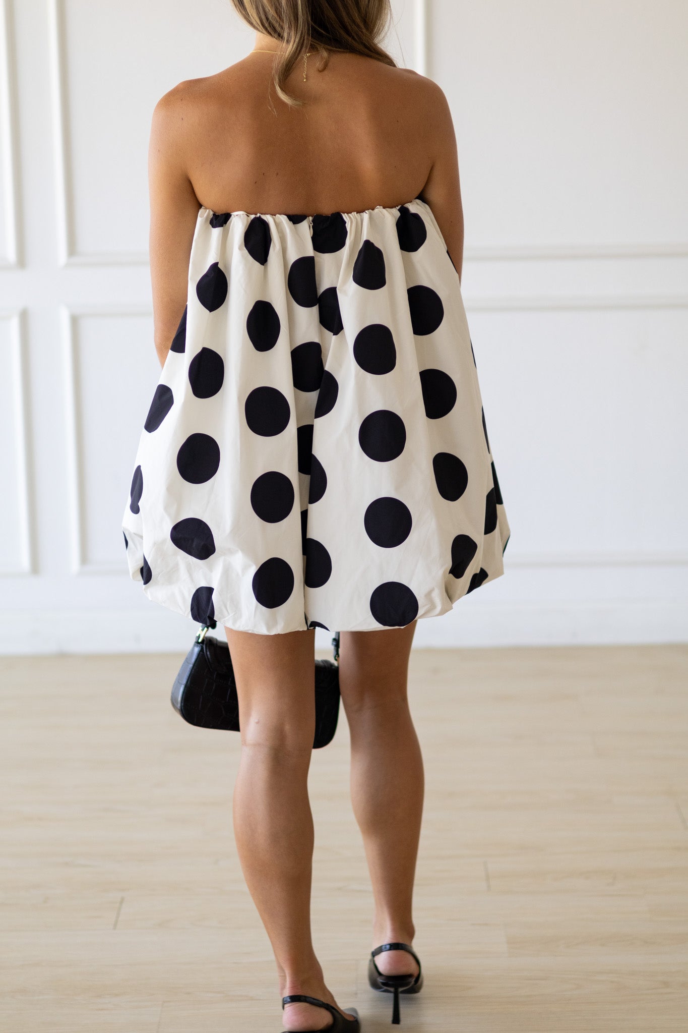 Woman wearing a strapless polka dot dress with black dots on a white background