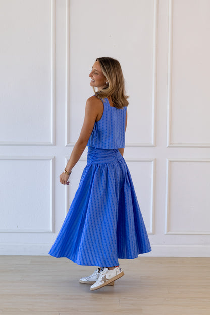 Woman wearing a blue dress standing against a white paneled wall.