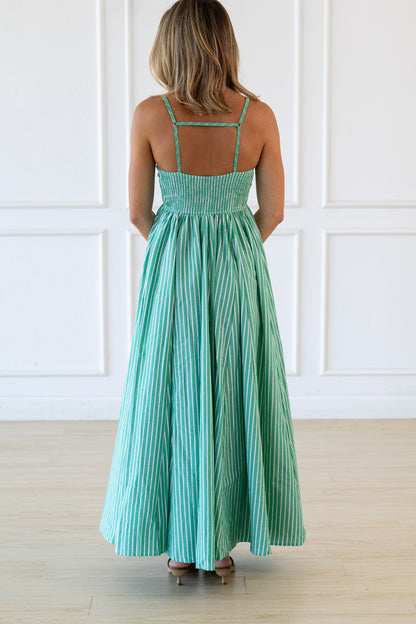 Woman wearing a green striped dress against a white paneled wall.
