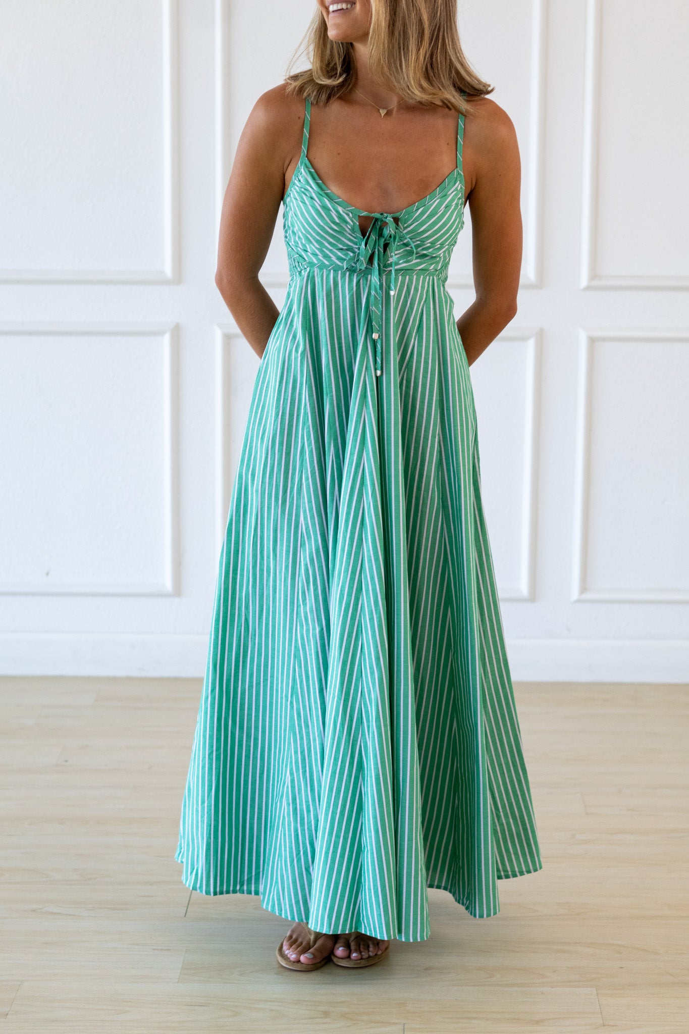 Woman wearing a green and white striped dress against a white paneled wall.