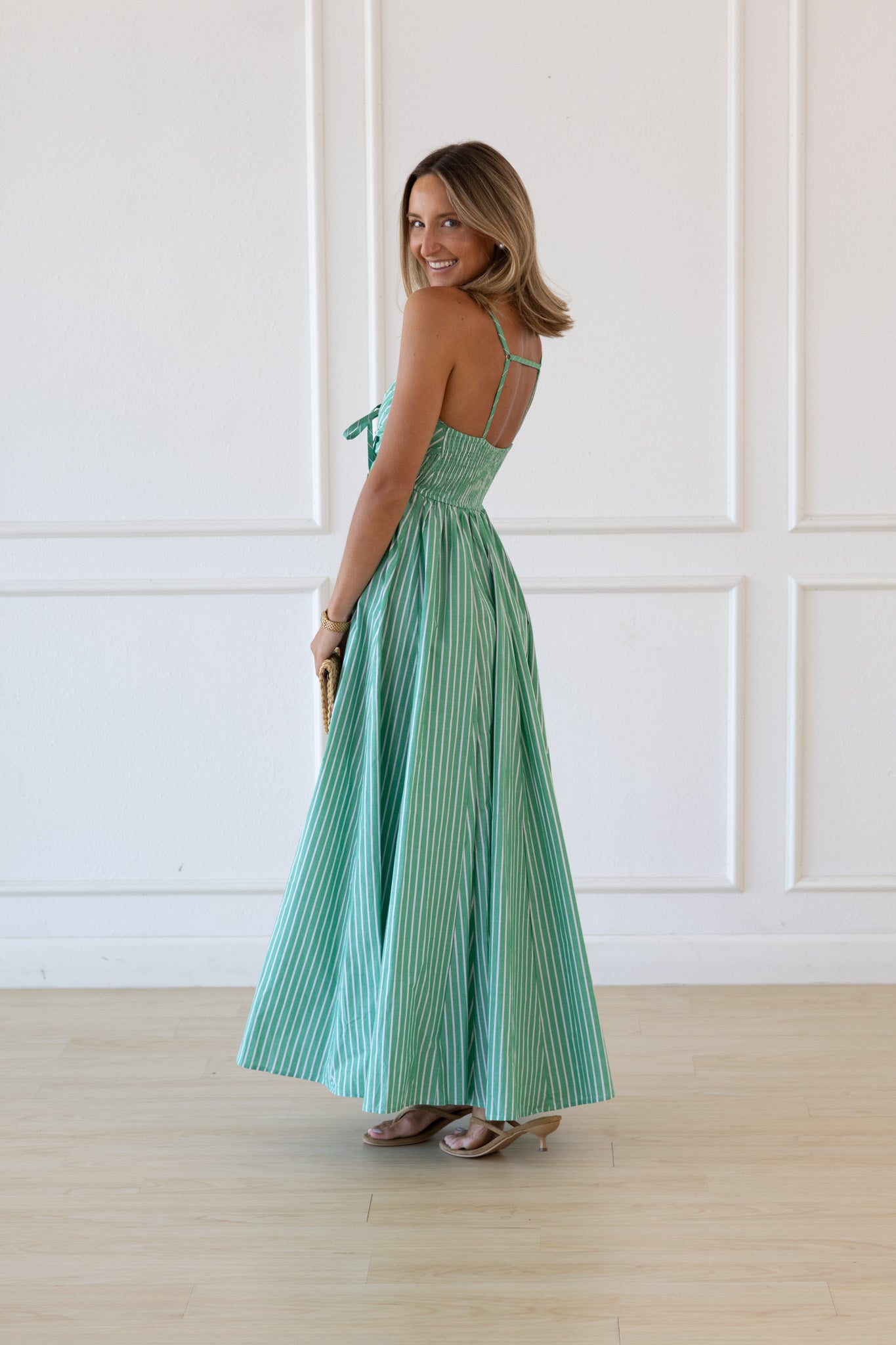 Woman wearing a green dress standing against a white paneled wall.