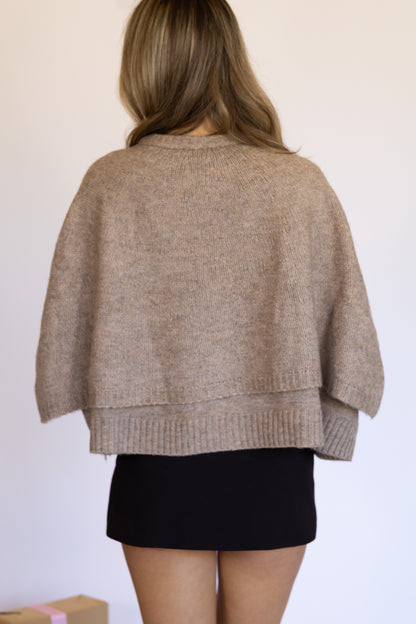 Person wearing a beige sweater over a black skirt on a plain background