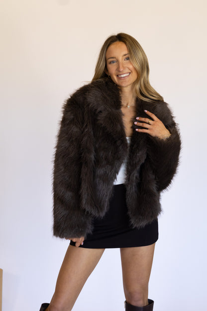 Woman wearing a dark brown fur coat against a plain background
