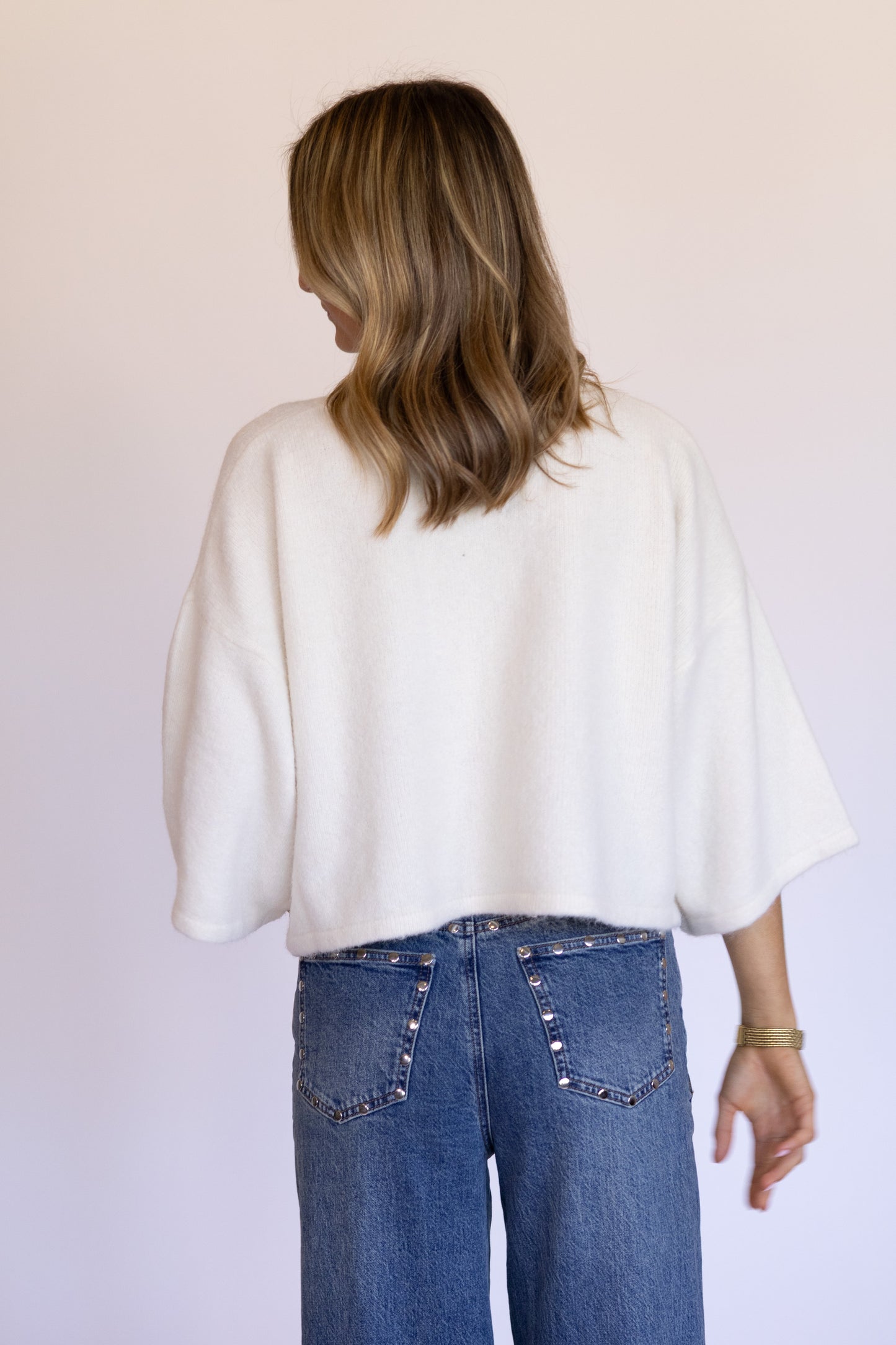 Person wearing a white top and blue jeans against a plain background