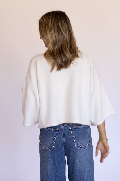 Person wearing a white top and blue jeans against a plain background