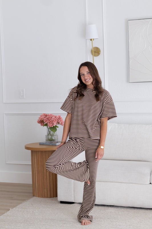 Woman in striped pajama set sitting on a couch in a living room.