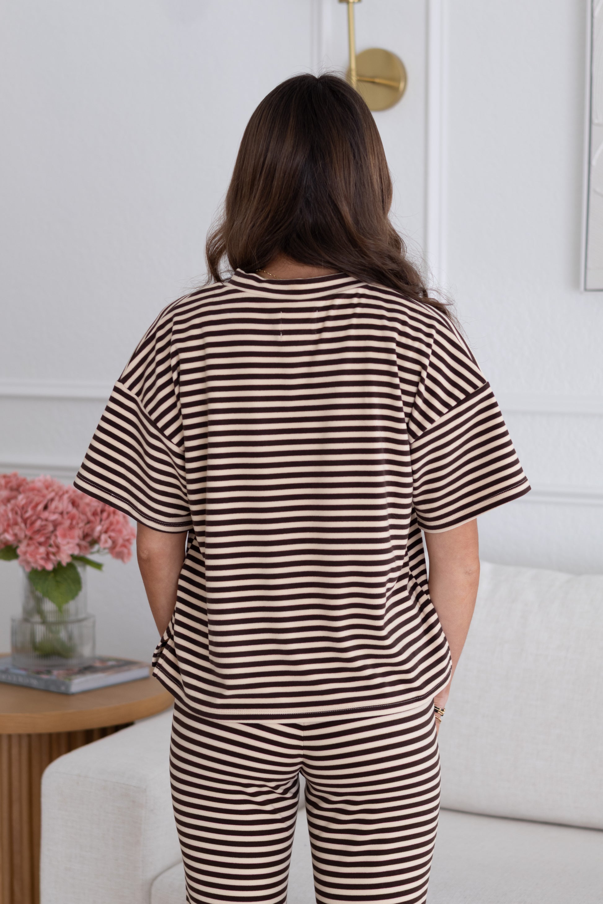 Person wearing a striped outfit standing in a room with a table and flowers.