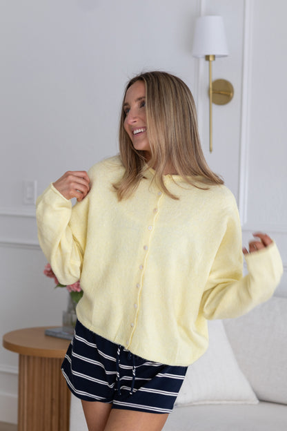 Woman wearing a yellow shirt and striped shorts in a room with a lamp and table.