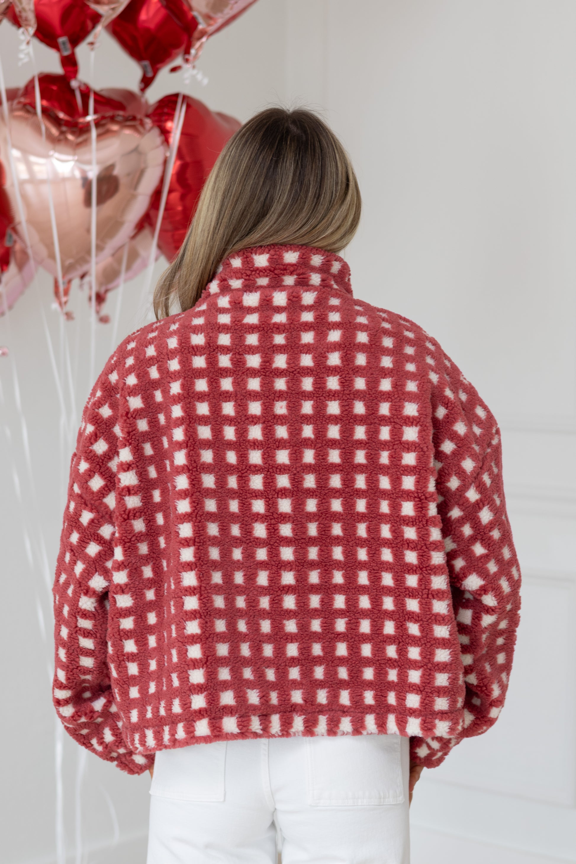 Person wearing a red and white checkered jacket with heart-shaped balloons in the background