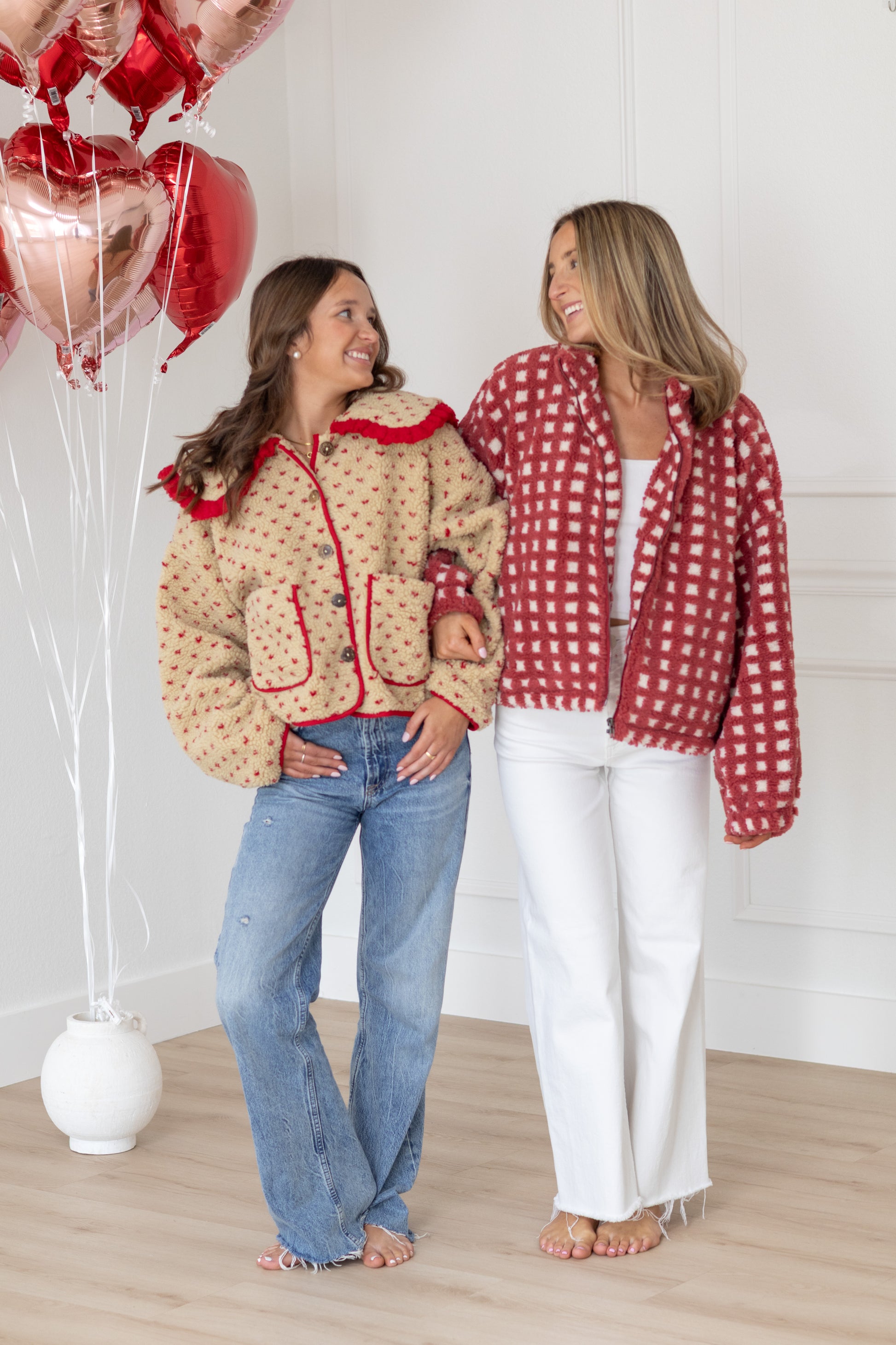 Two women wearing matching jackets with red and white patterns, standing indoors.