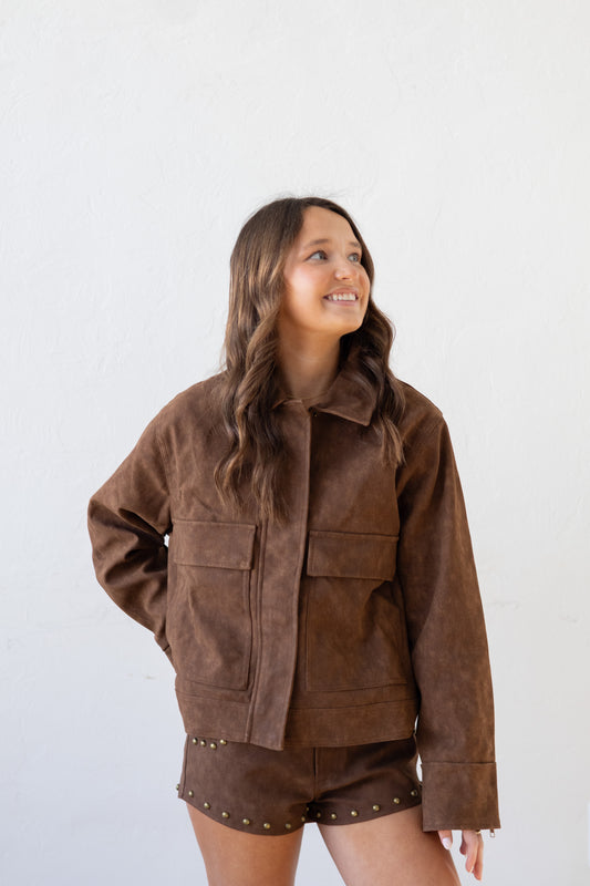 Woman wearing a brown suede jacket and shorts against a white background