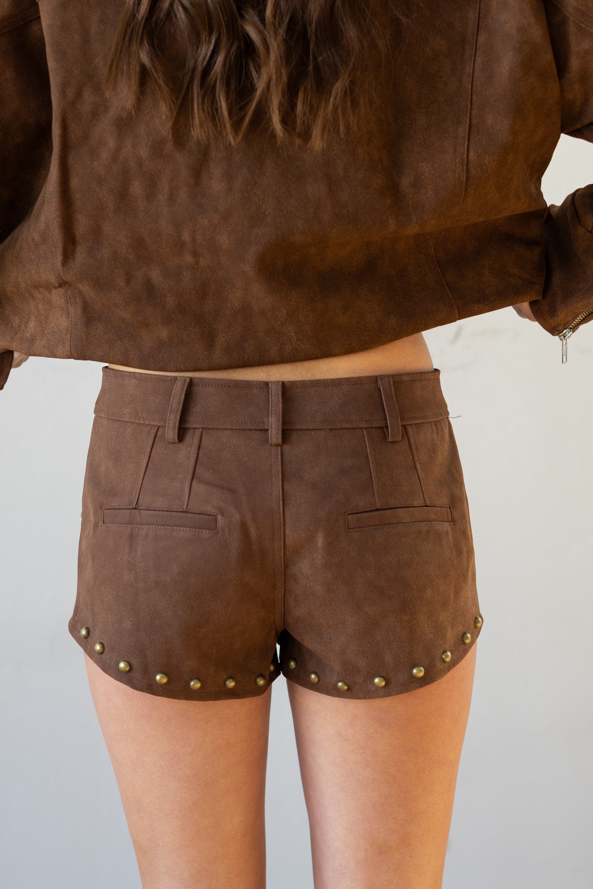 Person wearing brown leather shorts with gold studs on a plain background