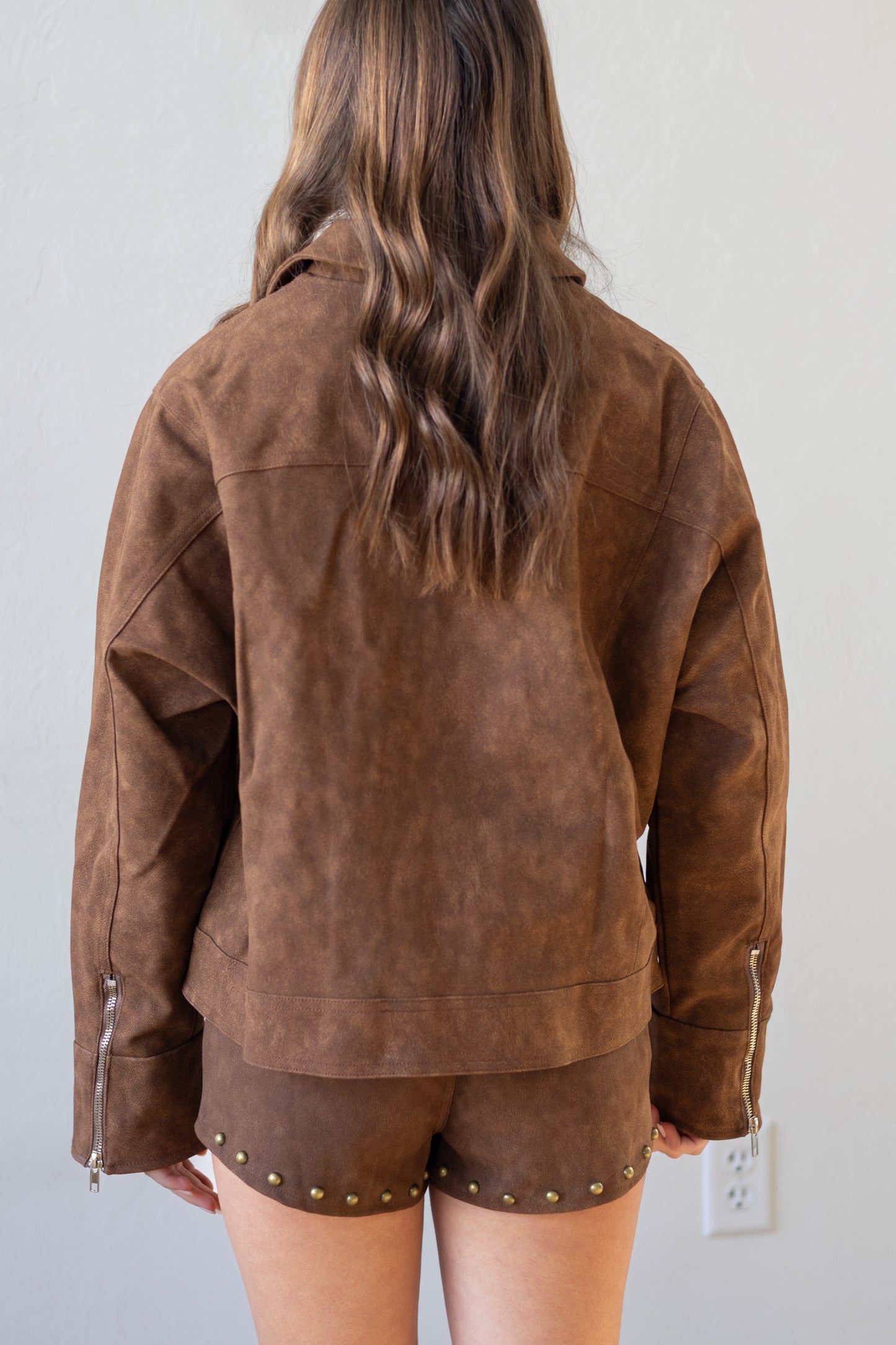 Person wearing a brown suede jacket and shorts against a plain background