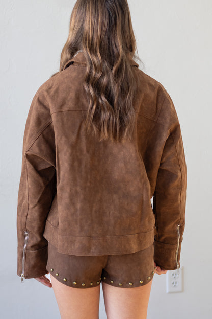 Person wearing a brown suede jacket and shorts against a plain background