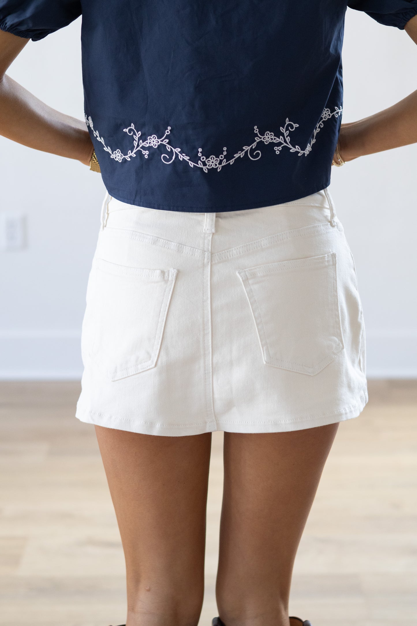 Person wearing a navy blue top with white embroidery and white shorts against a plain background