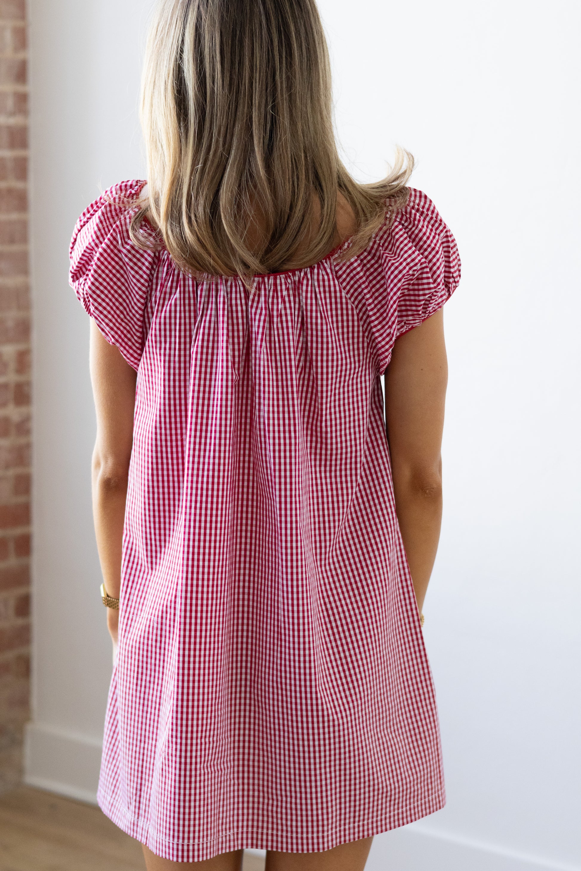 Person wearing a red and white checkered dress against a white wall.