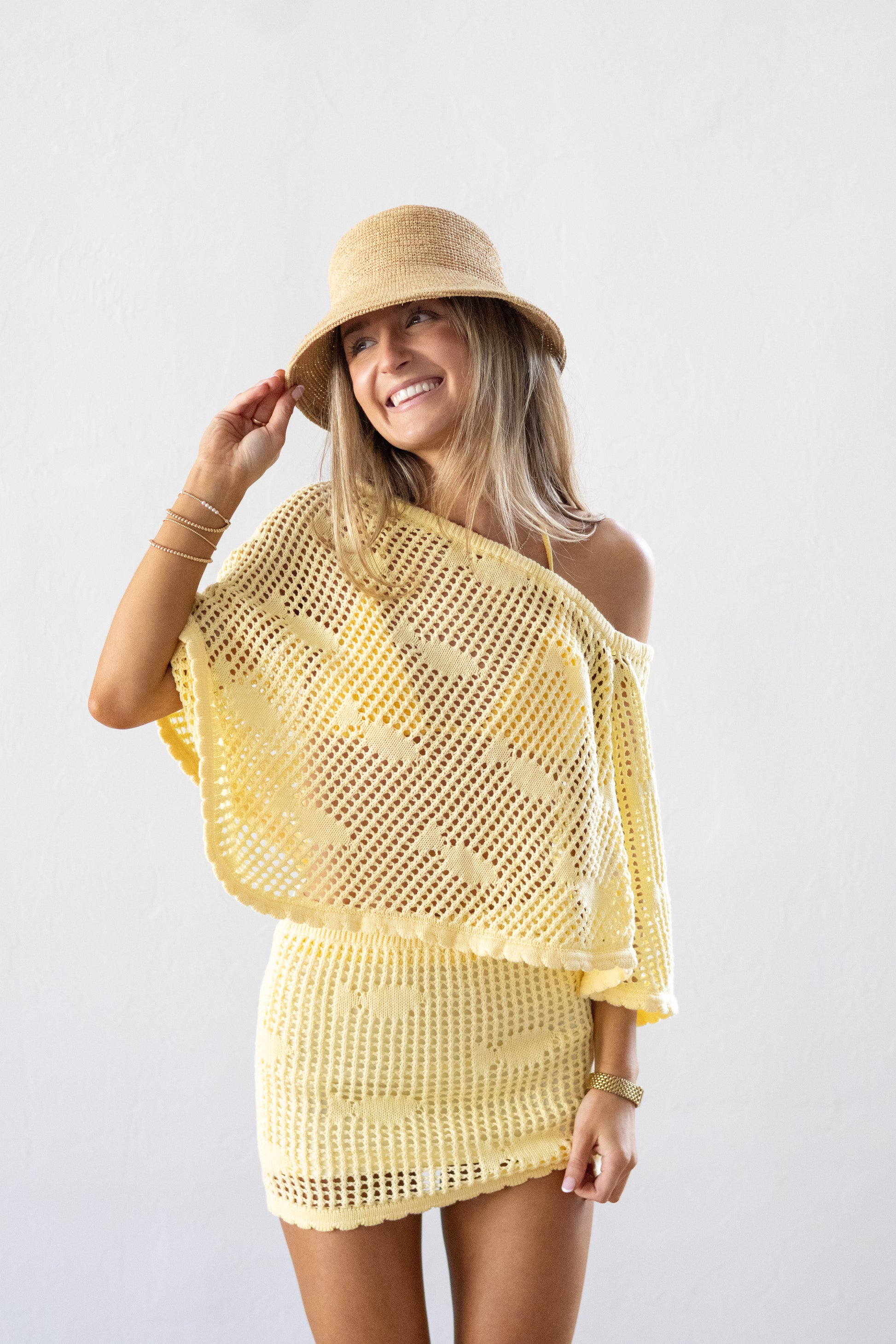 Woman wearing a yellow crochet cover-up and hat on a white background