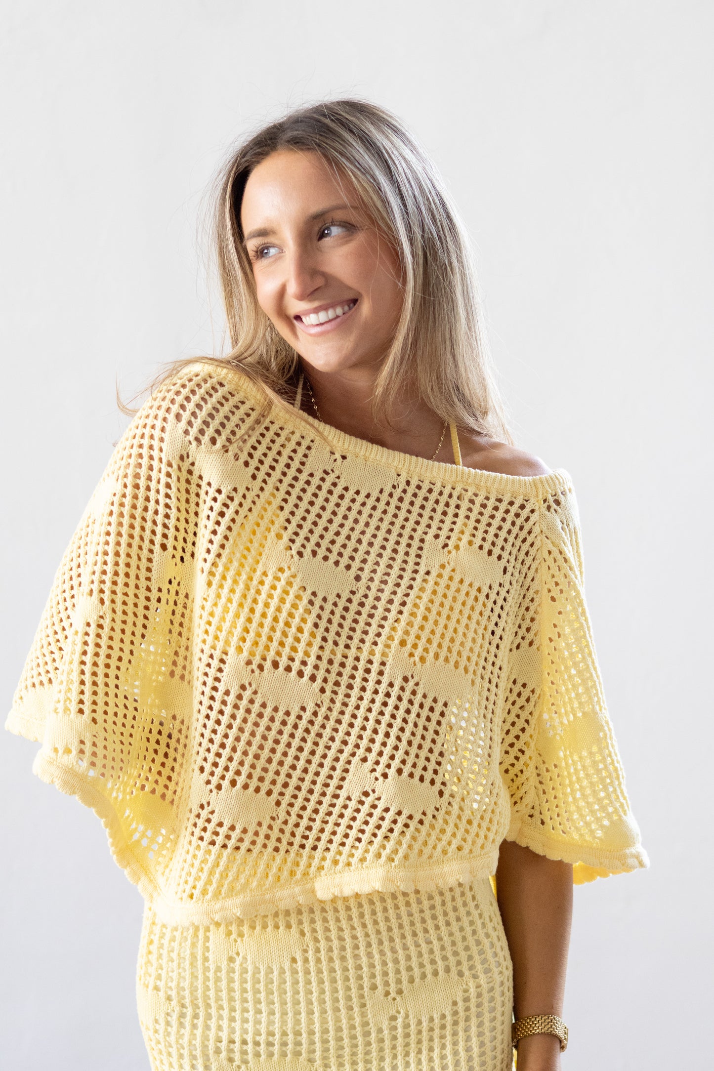 Woman wearing a yellow crochet top against a white background
