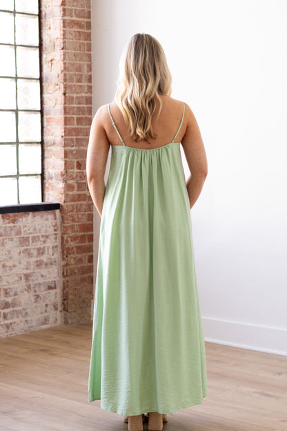 Woman wearing a light green dress standing in a room with brick walls and large windows.