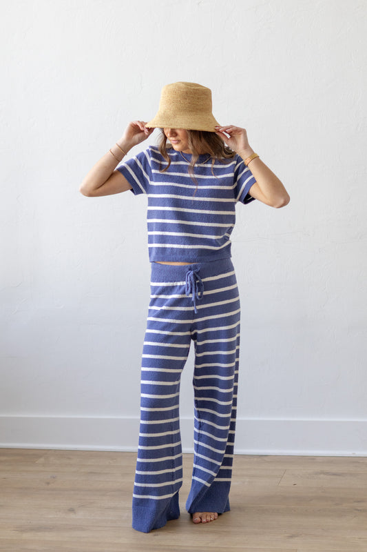 Person wearing a blue and white striped outfit with a straw hat against a plain background