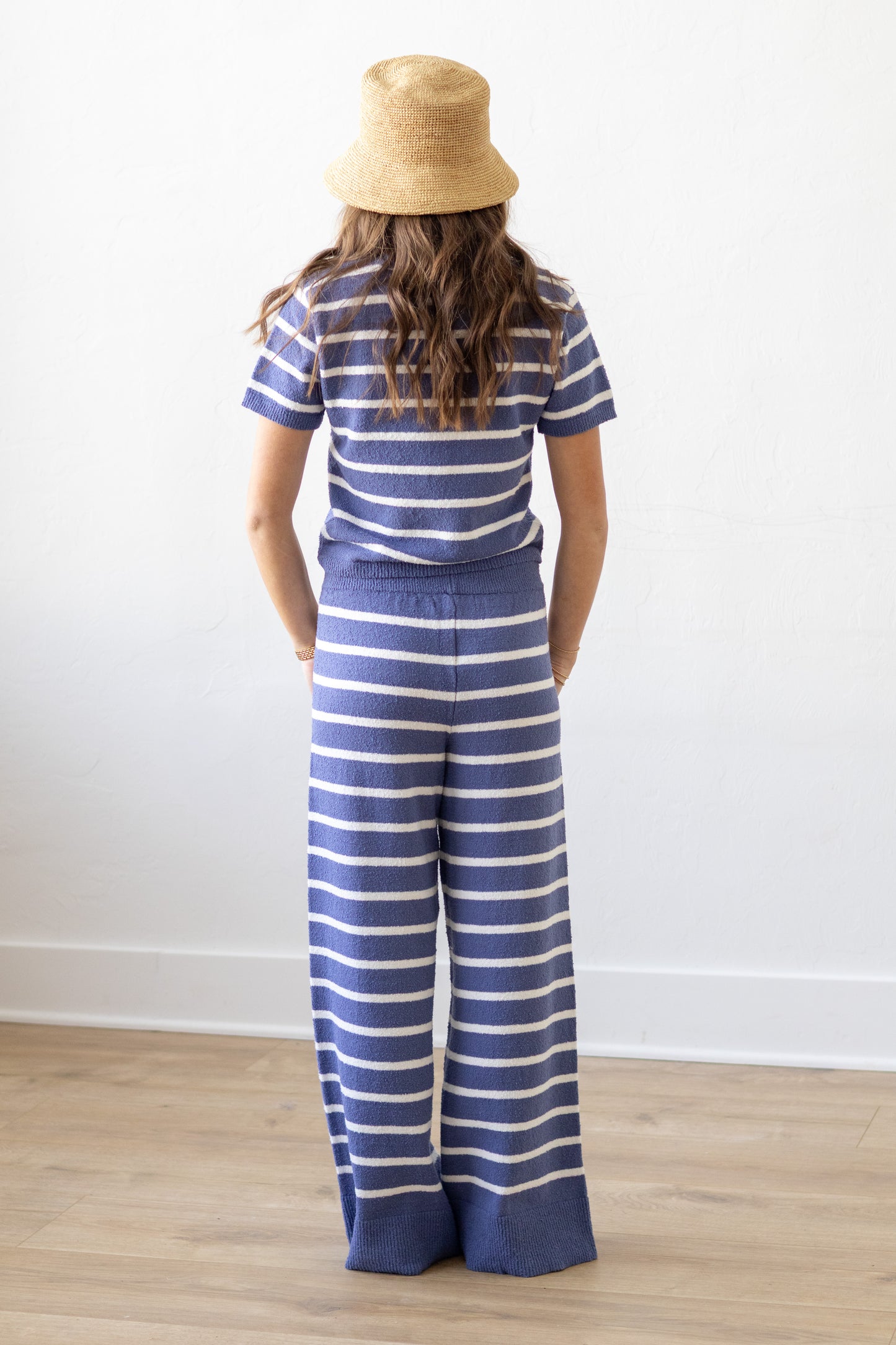 Person wearing a blue and white striped shirt and wide-leg pants, standing against a white wall.