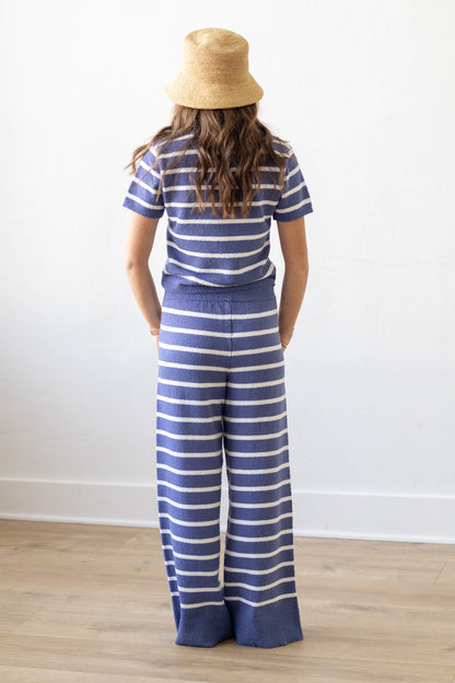 Person wearing a blue and white striped shirt and wide-leg pants, standing against a white wall.