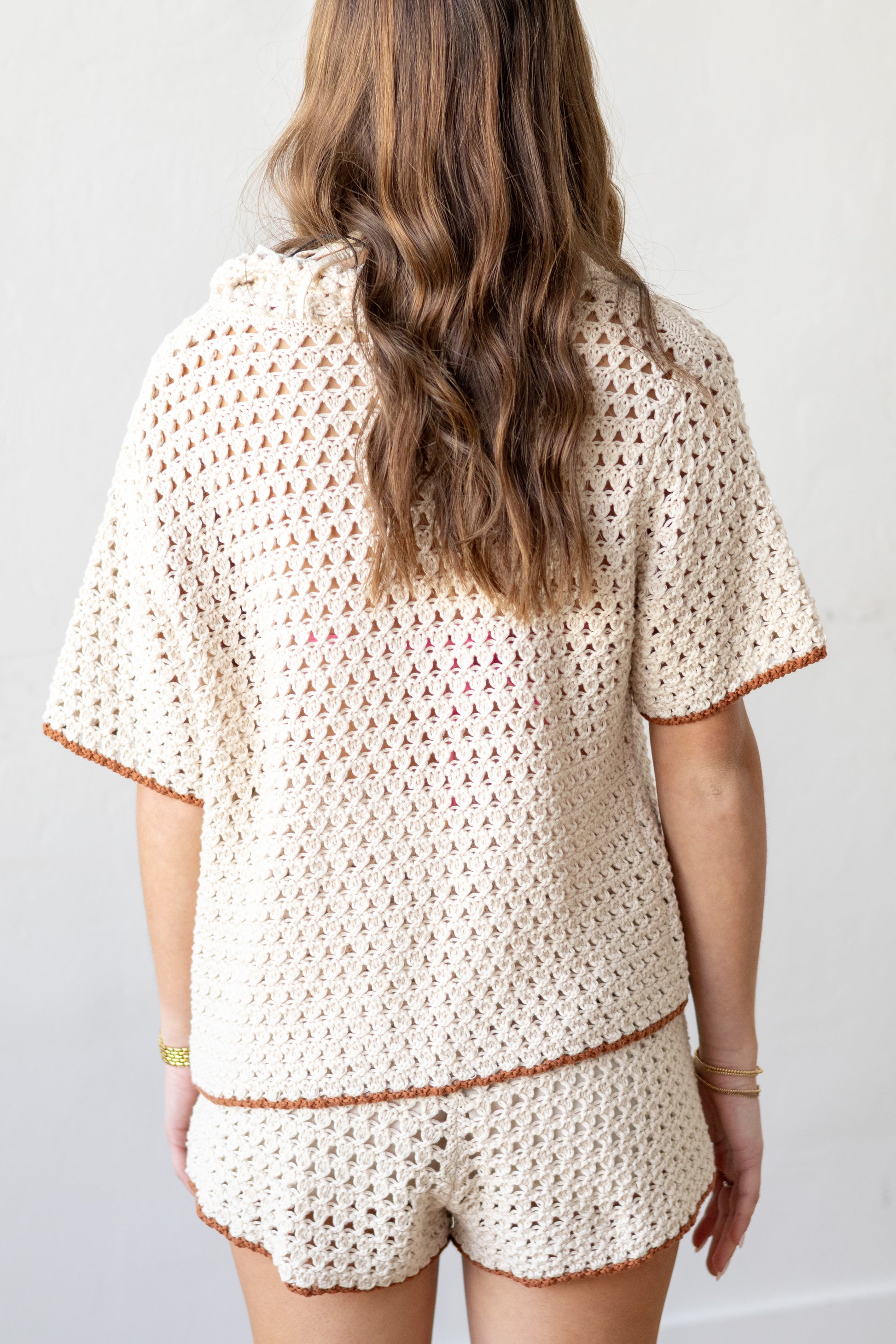 Person wearing a beige crochet top and shorts set against a white background