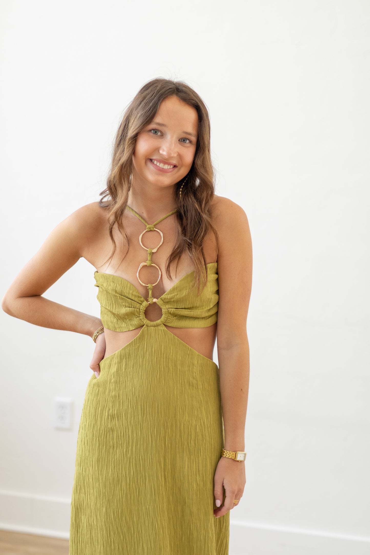 Woman wearing a green dress with cut-out design and gold necklace against a white background