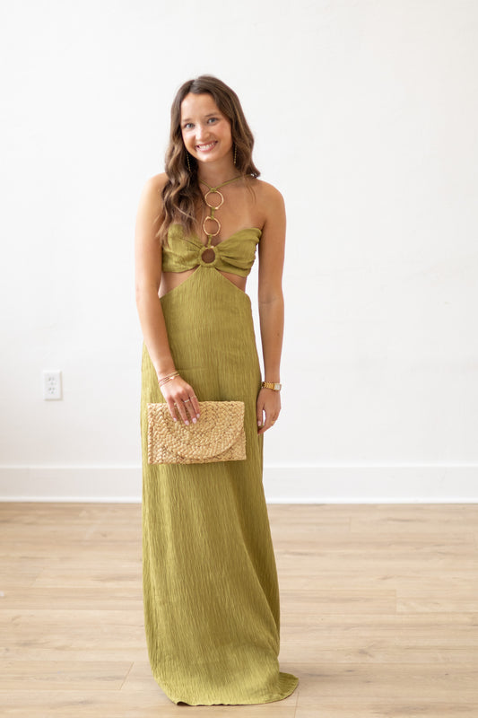 Woman wearing a green strapless dress with cut-out design, holding a gold clutch, on a white background.