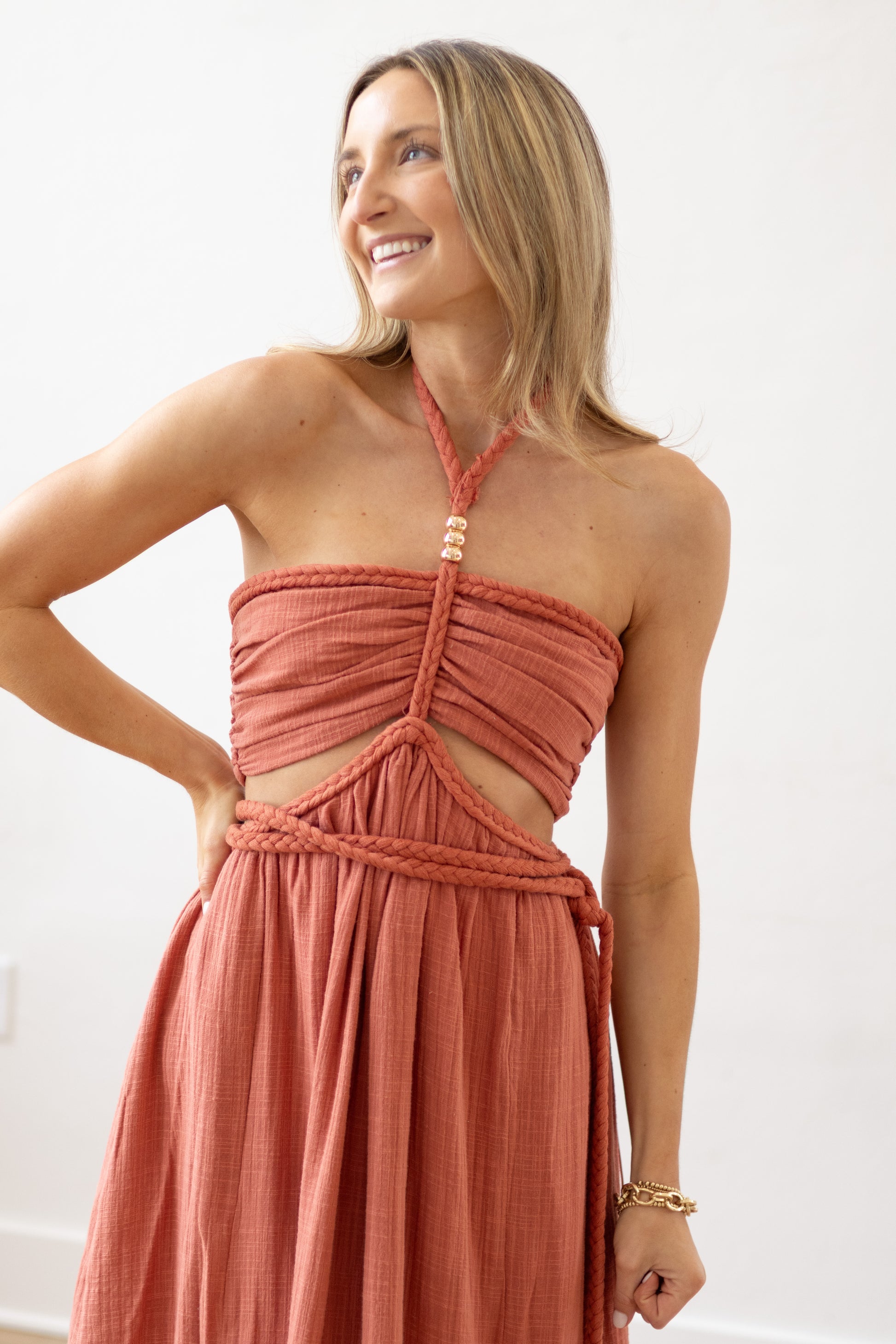 Woman wearing a coral halter neck dress with cut-out design against a white background