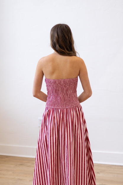 Woman wearing a red and white striped strapless dress against a white wall.