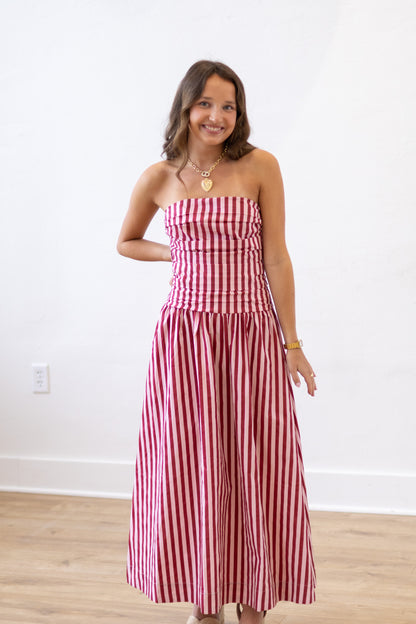 Woman wearing a red and white striped dress against a white wall.