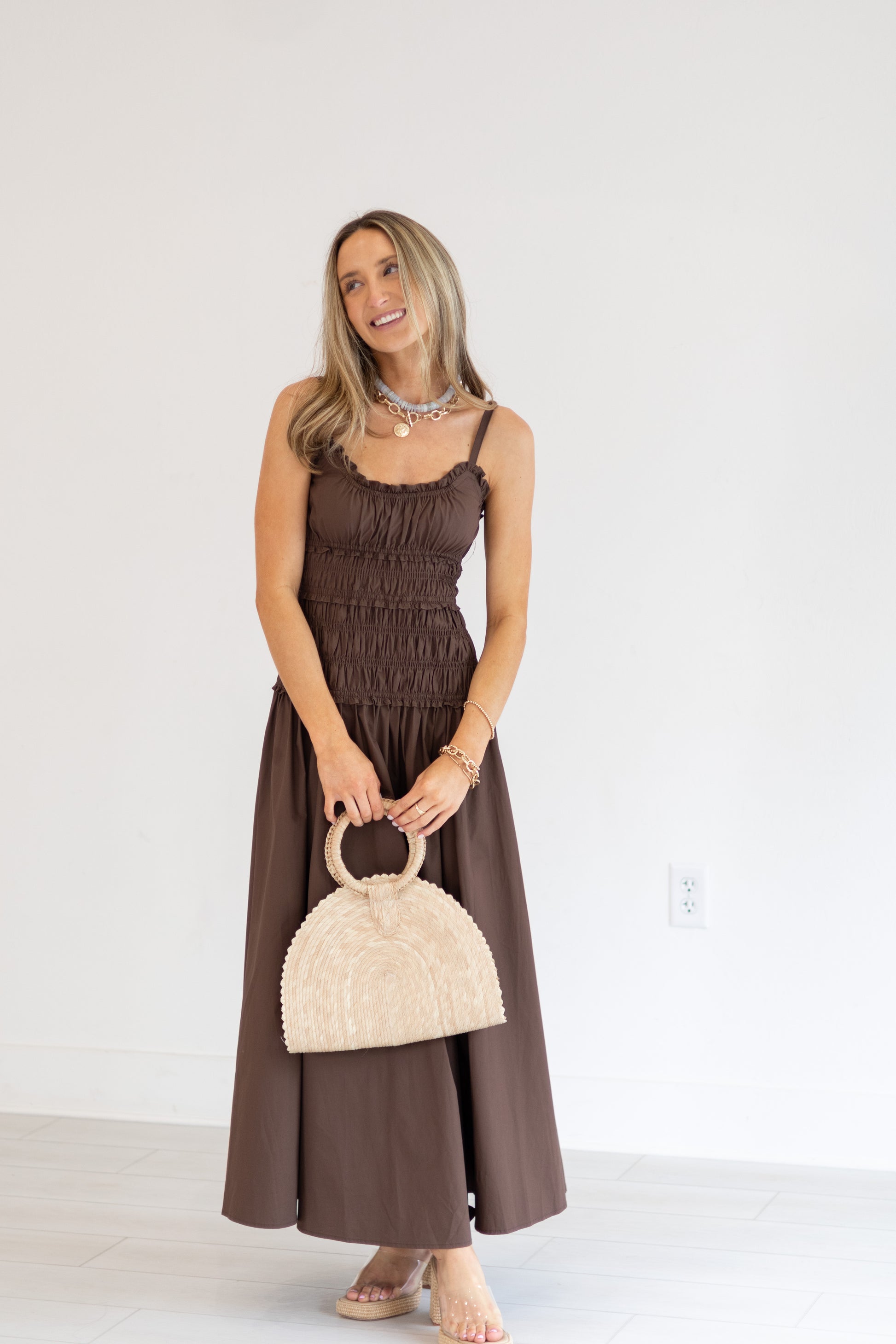 Woman in a brown dress holding a beige handbag against a white background