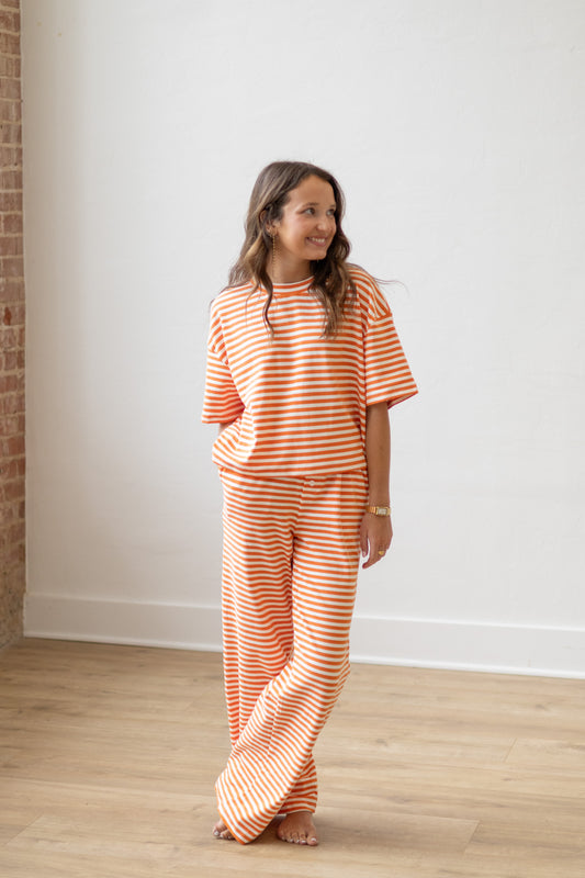 Woman wearing an orange and white striped outfit standing against a white wall.
