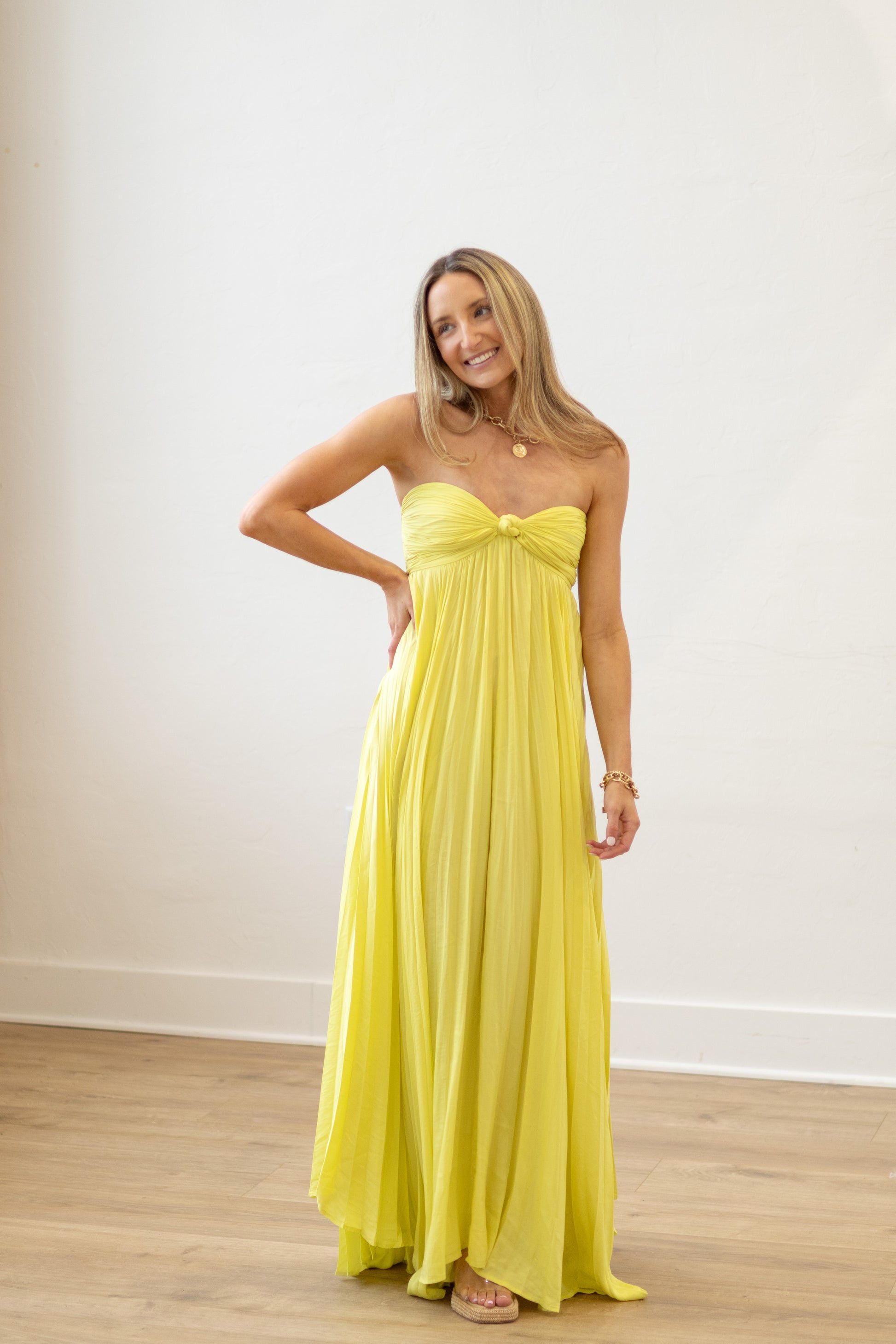 Woman wearing a yellow strapless gown against a white wall.