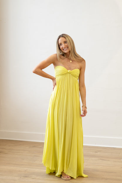Woman wearing a yellow strapless gown against a white wall.