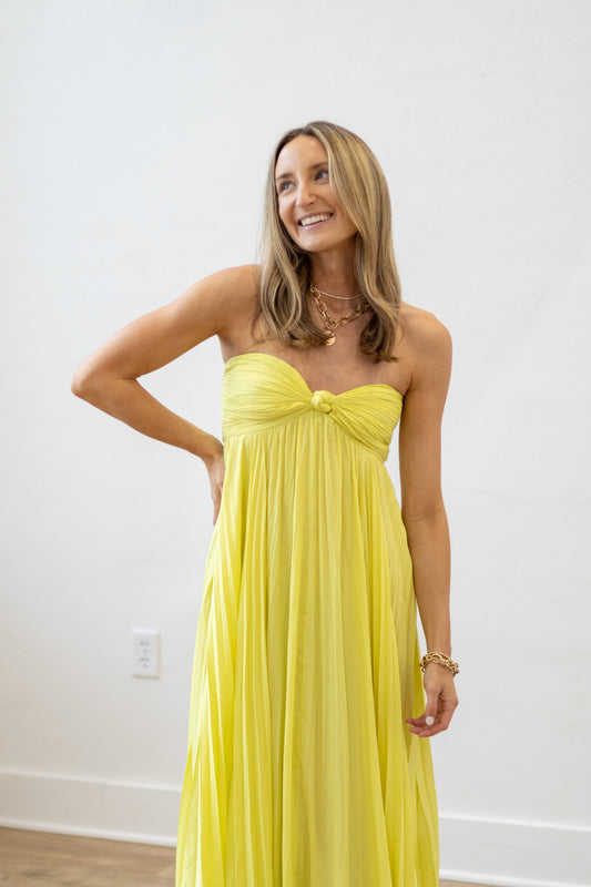Woman wearing a yellow strapless dress against a white wall.