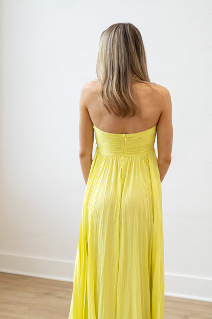 Woman wearing a yellow strapless dress against a white wall.