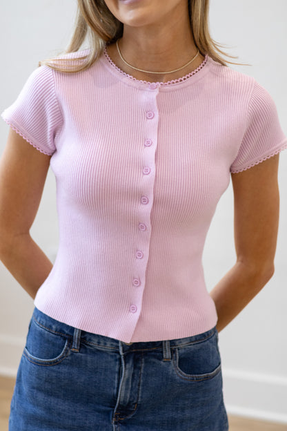 Person wearing a pink ribbed knit top with short sleeves and blue jeans.