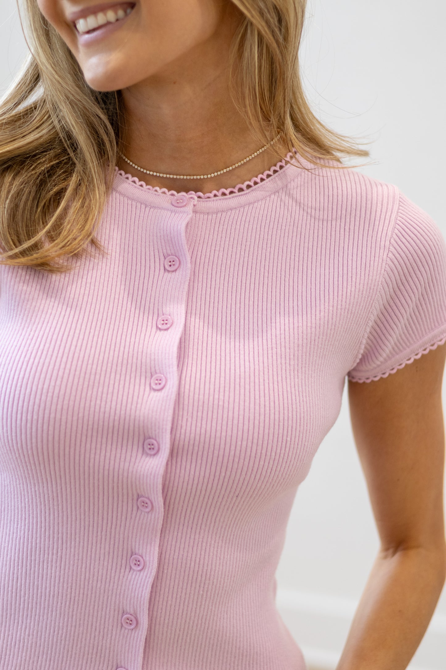 Woman wearing a pink ribbed top with buttons on a plain background