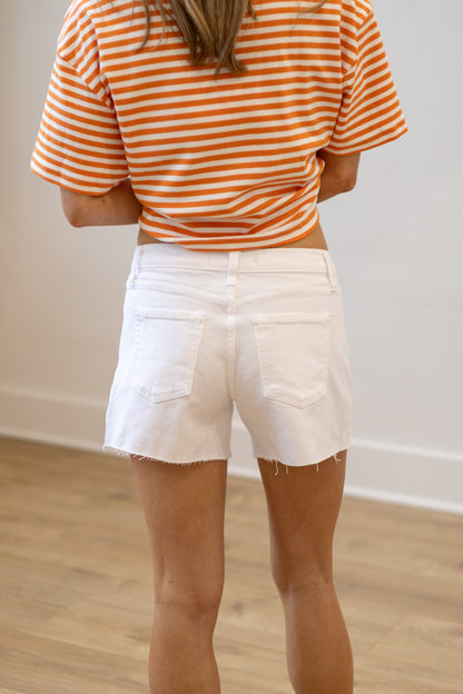 Person wearing an orange and white striped shirt and white shorts in a minimal indoor setting.