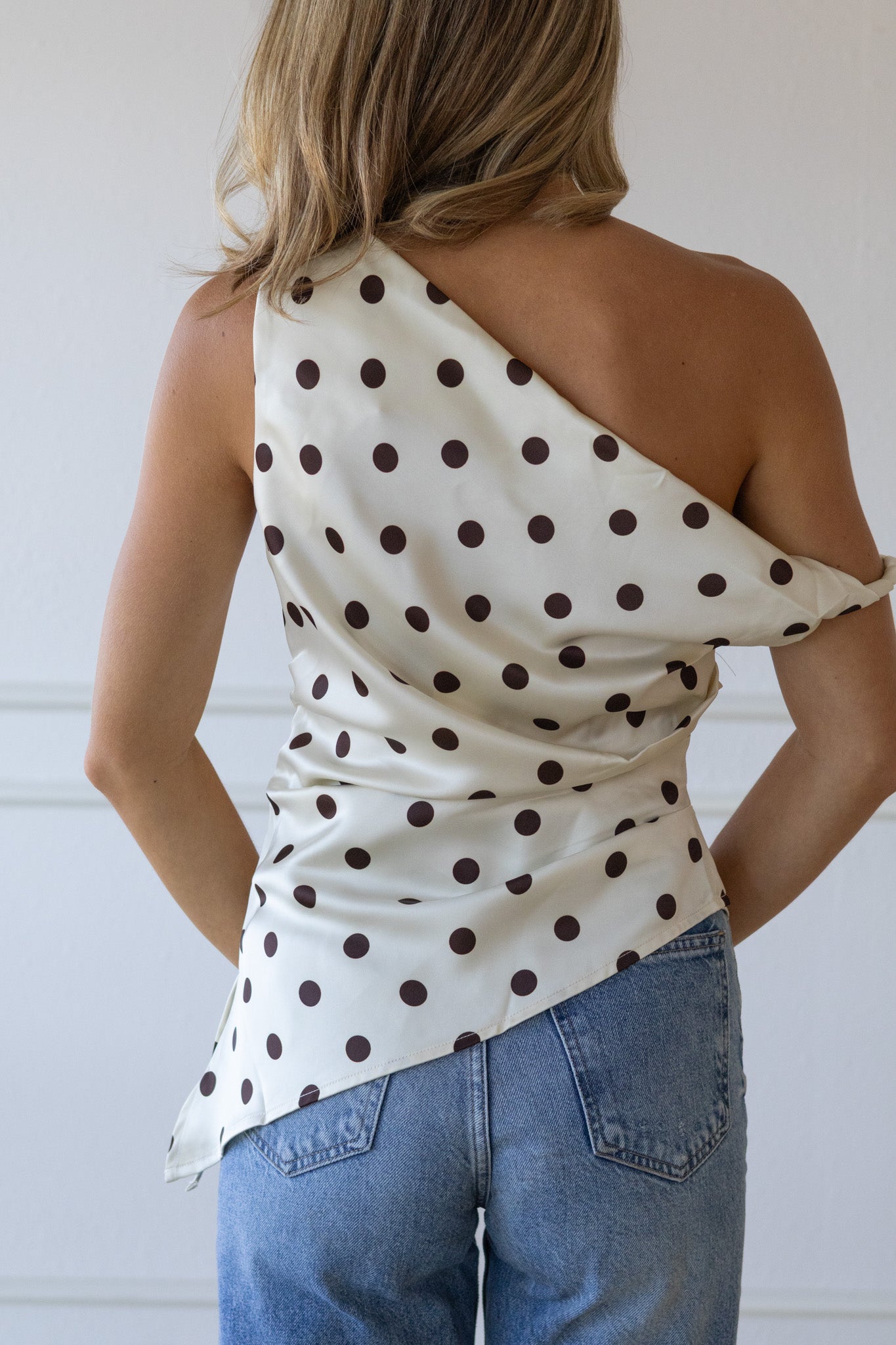 Woman wearing a polka dot one-shoulder top and jeans against a white background
