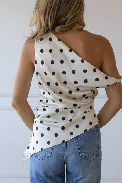 Woman wearing a polka dot one-shoulder top and jeans against a white background