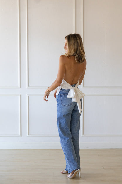 Woman wearing a white top and blue jeans with a white wall background